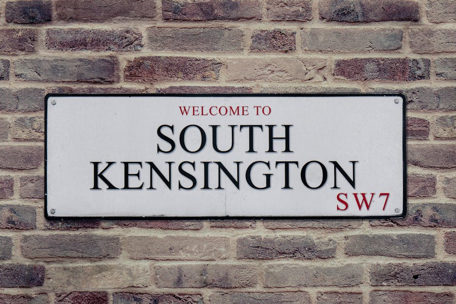 A rectangular white metal street sign mounted on a red-brown brick wall displaying the words 'WELCOME TO SOUTH KENSINGTON' in bold black uppercase letters, with 'WELCOME TO' and 'SW7' printed in small